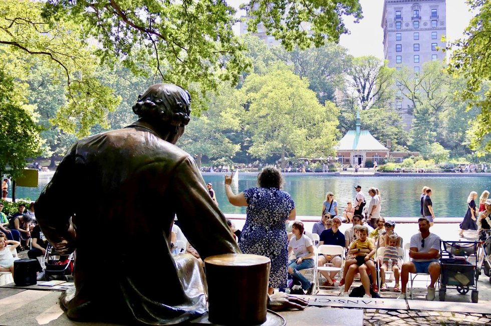 Storyteller performing in front of a crowd at the Hans Christian Andersen statue, with Conservatory Water in the background