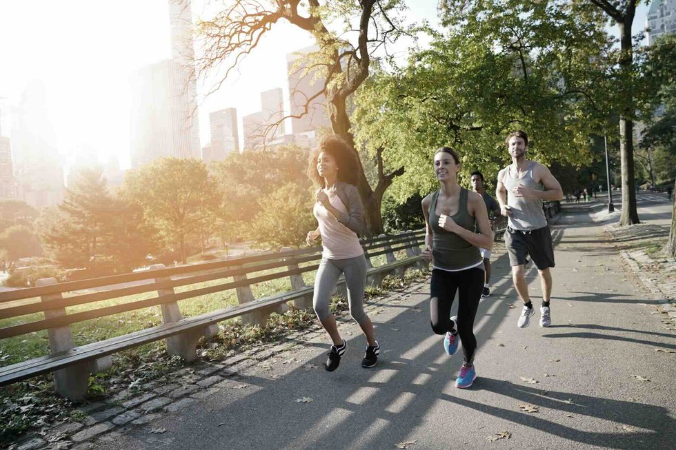 Runners jogging on a path in Central Park with the city skyline and morning sun in the background
